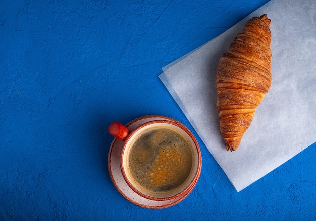 Café dans une tasse et croissant sur une table bleue