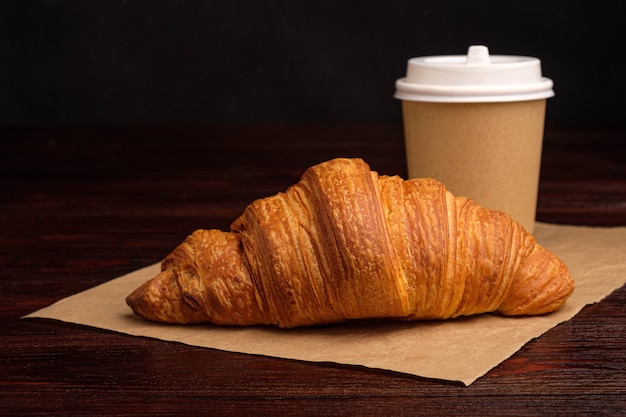 Café dans une tasse en papier et croissant sur table en bois