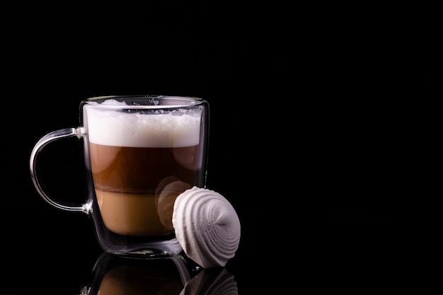 Café dans une tasse en verre et guimauves placées contre la tasse.