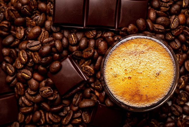 Café dans une tasse en verre sur une table en bois. Grains de café et morceaux de chocolat.