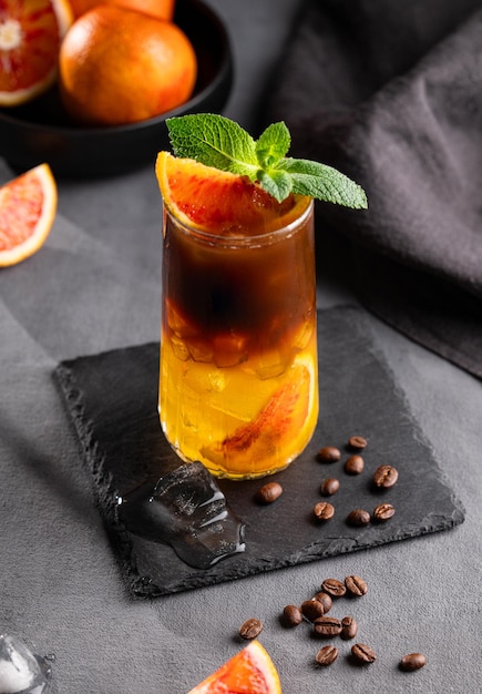 Café avec du jus d'orange dans un grand verre avec de la glace et de la menthe sur un fond sombre