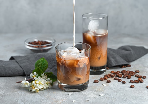 Café avec du lait et de la glace sur un mur gris. Verser le lait dans un verre de café glacé.