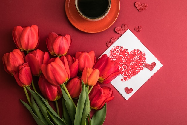 Café du matin et bouquet de tulipes rouges sur une surface rouge vif