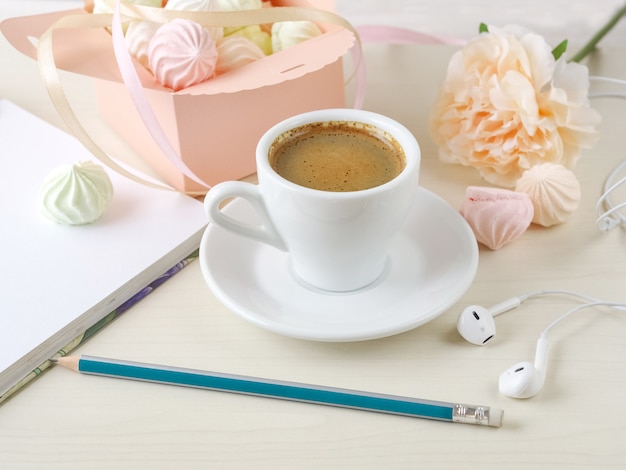 Café du matin avec un cahier et une boîte remplie de petites meringues sur un fond clair en bois