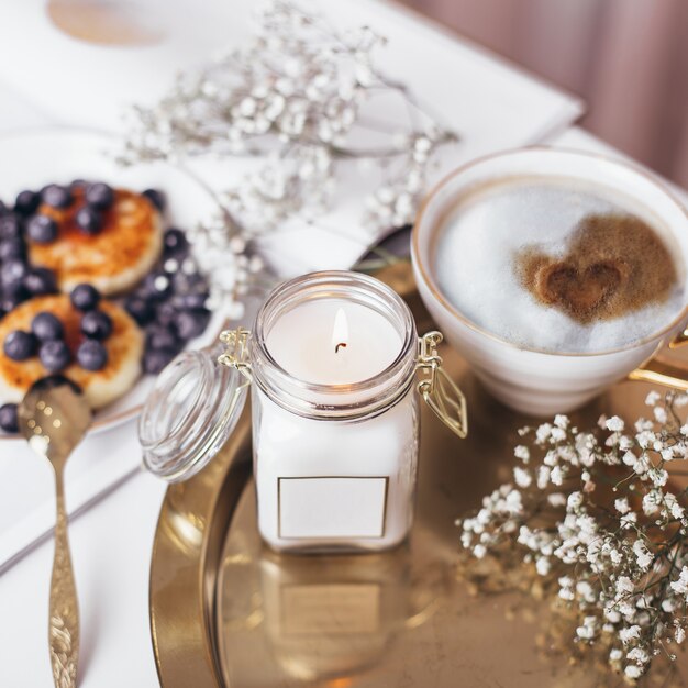 Café du matin et gâteaux au fromage avec des myrtilles décorées de fleurs et de chandelles sur plaque dorée