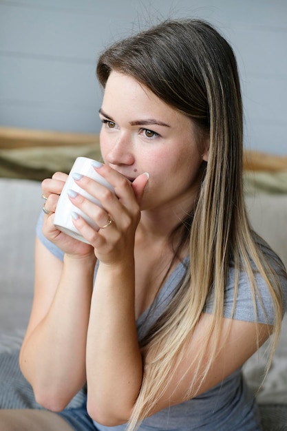 Café du matin jeune belle femme boit du café au lit portrait photo verticale