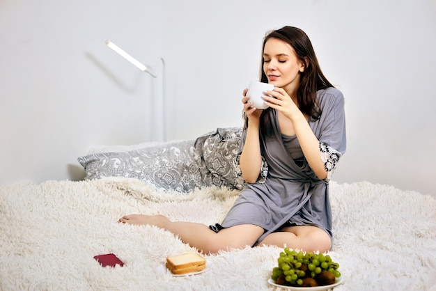 Café du matin pour jeune femme en déshabillé qui est assise dans son lit à l'intérieur