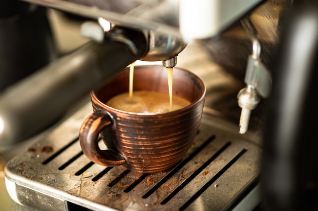 Le café est préparé dans une machine à café. Le café fraîchement préparé est versé dans une tasse en terre cuite.