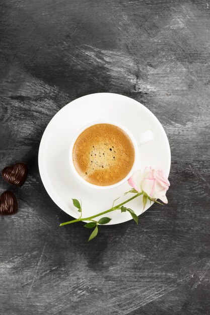 Café expresso dans une tasse blanche, une rose rose et des chocolats sur fond sombre. Vue de dessus. Contexte alimentaire.