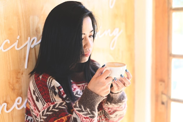 Café de femme avec la main tenant une tasse au café jeune femme buvant du café ou du thé femme détendue sentant le café à la maison en hiver avec une tasse de café