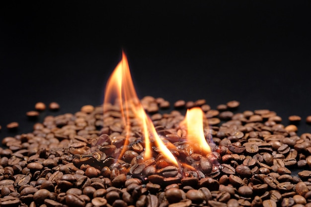 Café en feu sur fond noir gros plan de grains de café torréfiés épars