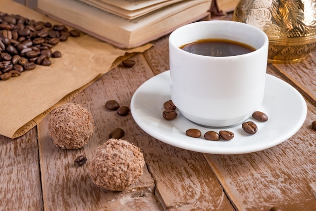 Café frais broyé dans la boisson du matin cezve dans une tasse blanche à côté de boules de chocolat