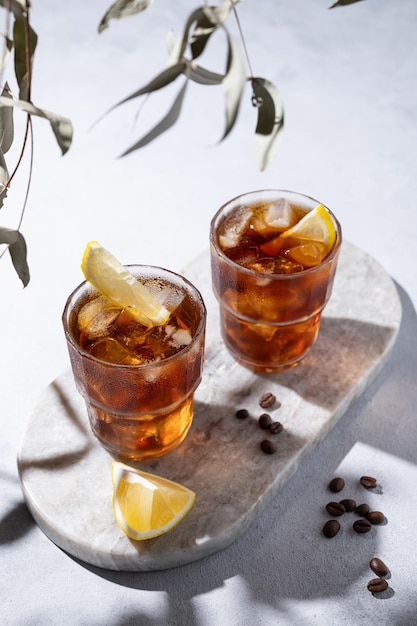 Café froid dans deux verres avec du citron et de la glace sur une planche de marbre sur un fond clair avec des grains de café et des ombres Concept d'artisanat d'été boisson rafraîchissante faite maison