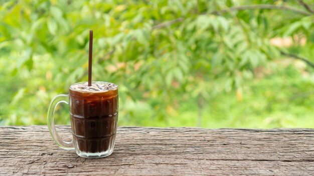 Café glacé Americano sur une table en bois et nature verdoyante