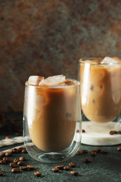 Café glacé dans un grand verre avec de la crème versé sur des glaçons et des haricots sur une table en béton sombre Boisson d'été froide avec des tubes sur un fond noir avec un espace de copie