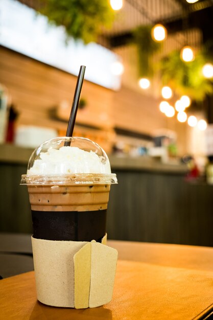 Café glacé dans une tasse à emporter sur la table en bois avec fond de café café floue, mise au point sélective