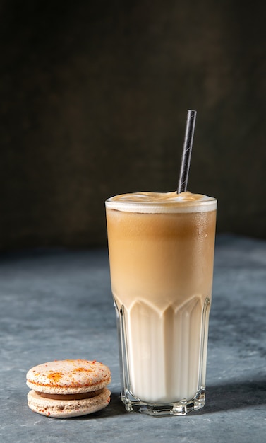 Café glacé dans un verre avec du lait versé et macaron sur une vieille table grise rustique boisson d'été froid latte