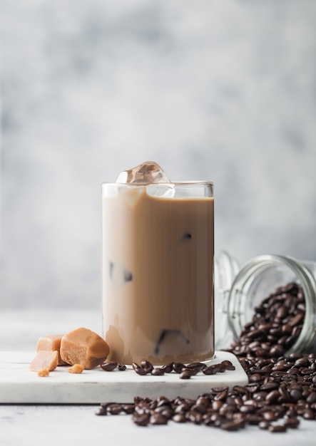 Café glacé froid avec du lait en verre avec pot de grains de café frais et caramel salé sur planche de marbre et fond clair