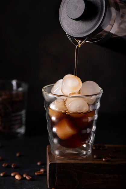 Le café glacé noir est versé dans un verre avec de la glace, sur fond noir