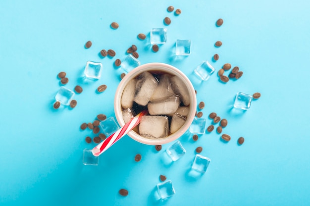 Café glacé rafraîchissant dans un verre et des glaçons et des grains de café sur une surface bleue. Concept d'été, cola avec de la glace, cocktail rafraîchissant, soif. Mise à plat, vue de dessus