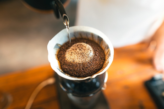 Photo café goutte à goutte, barista versant de l'eau sur du café moulu avec filtre, préparation du café