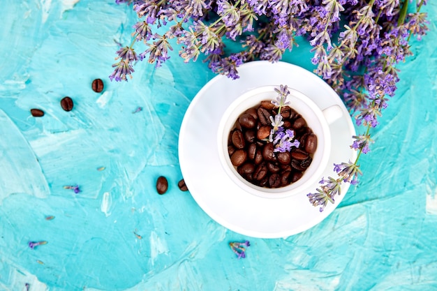 Café à grains dans des tasses et fleur de lavande sur fond bleu d'en haut.