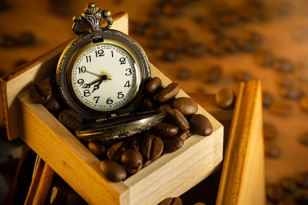 Café en grains et montre de poche dans un moulin manuel sur table