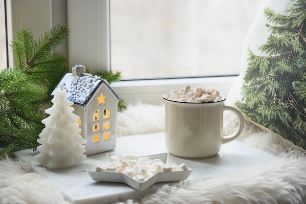 Café d'hiver avec guimauve sur le rebord de la fenêtre et peau de fourrure décorée de branches de sapin Noël