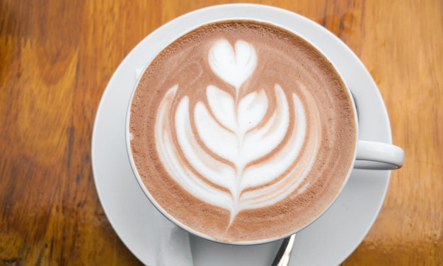 Café Latte d'art chaud dans une tasse sur une table en bois et un arrière-plan flou de café