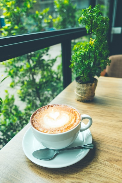 Café latte art avec petit arbre sur le bureau en bois au café couleur ton vintage