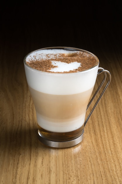 Photo café latte art avec sirop, lait et cannelle dans un verre transparent avec une poignée en métal sur une table en bois