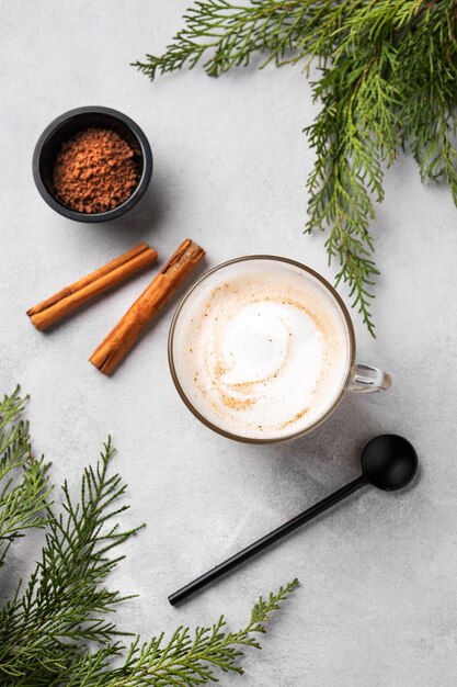 Café latte ou cappuccino épicé avec des bâtons de cannelle sur un fond clair avec des branches de sapin