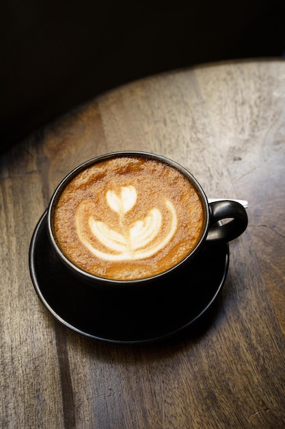 Photo café latte chaud avec de la mousse de lait latte art dans une tasse sur un bureau en bois en vue d'en haut comme petit déjeuner dans un café au cafeduring concept de travail d'affaires style vintage