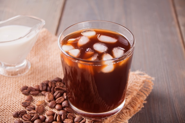 Café latte glacé avec des glaçons et des grains de café sur une table.