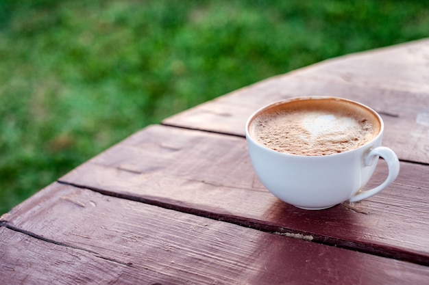 Café latte en tasse sur table en bois et pelouse verte