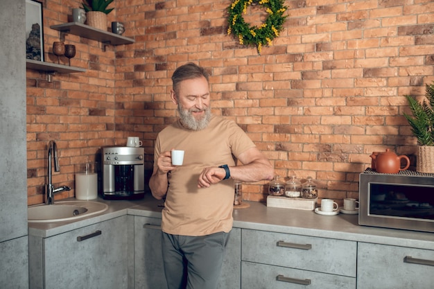 Café matinal. Un homme d'âge moyen debout dans la cuisine avec une tasse de café dans les mains