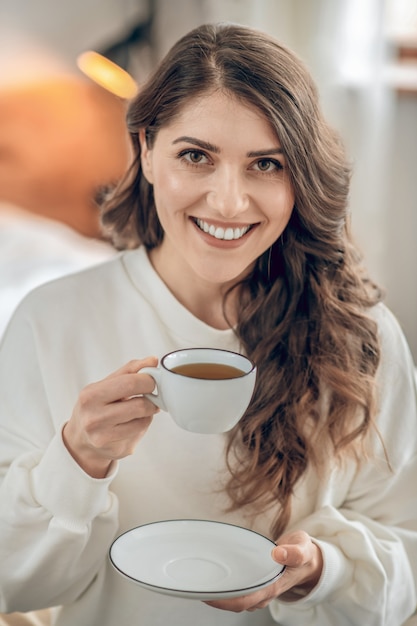 Café matinal. Jolie jeune femme assise sur le lit et buvant du café