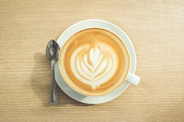 Un café avec des motifs de feuilles dans une tasse blanche sur fond en bois