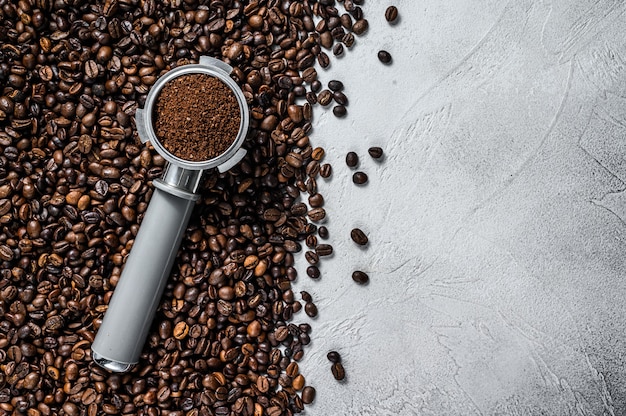 Café moulu dans le porte-filtre pour espresso avec des grains de café sur blanc. Vue de dessus.