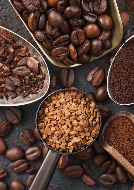 Café moulu et en grains et granulés de café instantané lyophilisés dans diverses cuillères et cuillères sur fond noir Vue de dessus