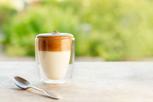 Photo café mousseux dalgona en verre avec cuillère sur table sur fond vert. tendance café au lait glacé coréen avec mousse de café instantané avec espace de copie pour le texte.