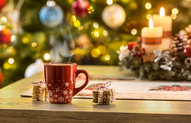 Café de Noël et couronne de l'Avent sur table avec des lumières bohème en arrière-plan.