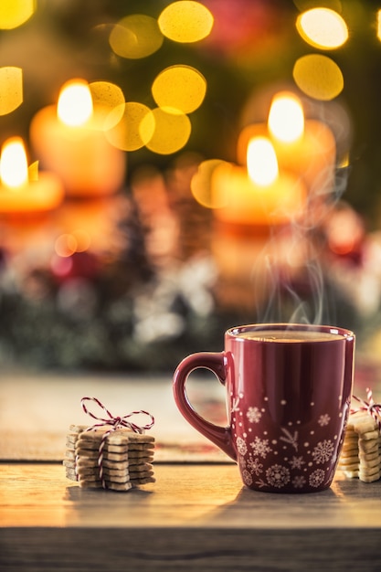 Café de Noël et couronne de l'Avent sur table avec des lumières bohème en arrière-plan.