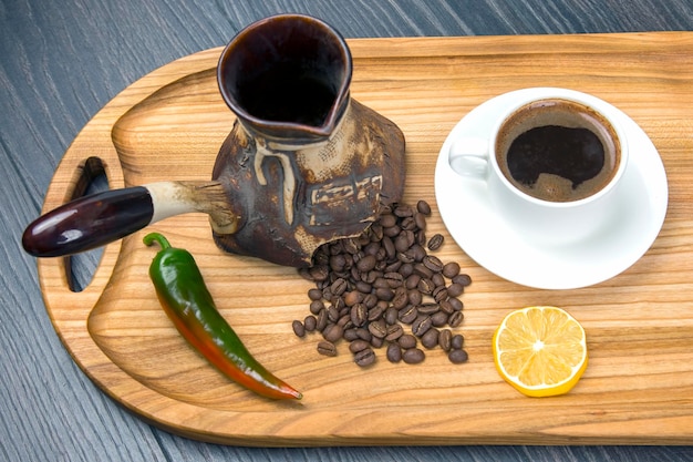 Café noir chaud fraîchement infusé dans une tasse blanche sur une planche de bois avec des grains de café piment et citron