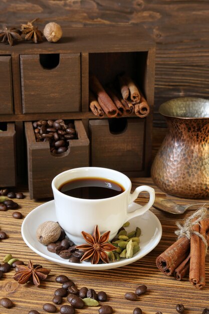 Café noir dans une tasse blanche et épices sur une table en bois