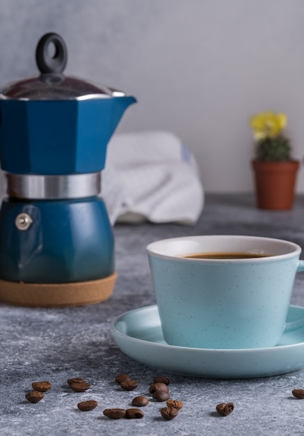 Café noir dans une tasse, cafetière geyser et grains de café sur une planche