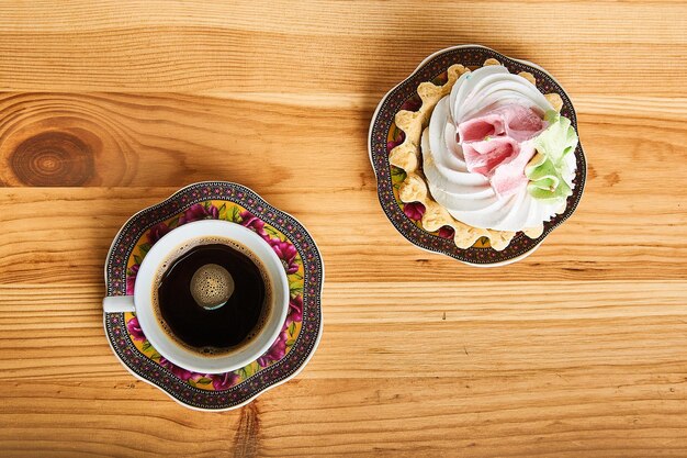 café noir sur petite tasse et gâteau avec crème protéinée sur fond de bois marron clair vue de dessus