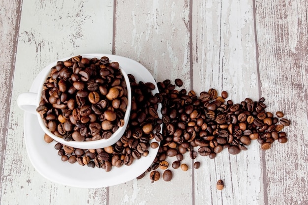 Café noir en tasse blanche et grains de café sur fond en bois clair.