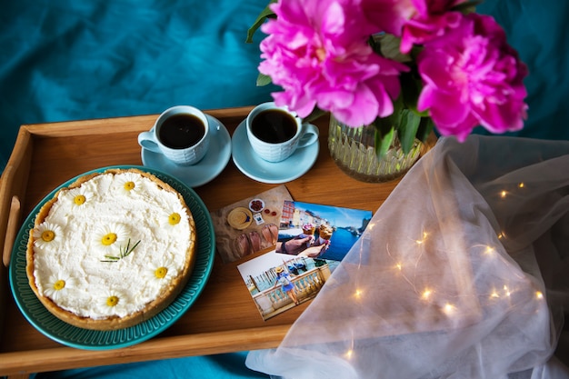 Café, pivoines roses, gâteau au fromage sur un plateau en bois, vue de dessus.