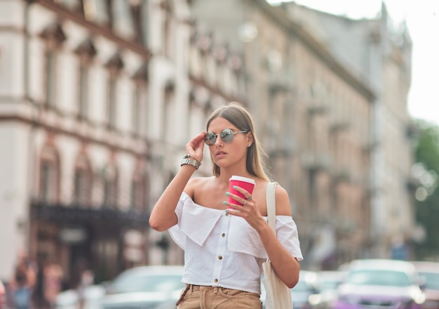 Café sur le pouce. Jeune femme de mode dans des vêtements d'été à la mode tenant une tasse de café en se promenant dans la ville